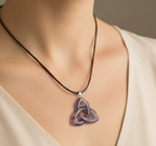 Colgante de amatista en forma de triqueta celta morada colgado de un cordón marrón sobre el cuello de una persona.