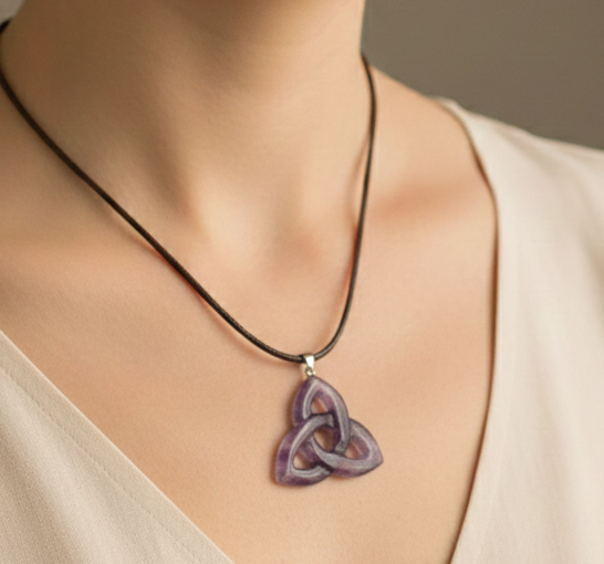 Colgante de amatista en forma de triqueta celta morada colgado de un cordón marrón sobre el cuello de una persona.
